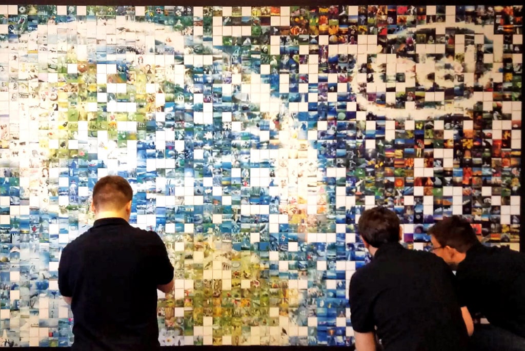 Three attendees placing their photos onto the Intel photo mosaic wall