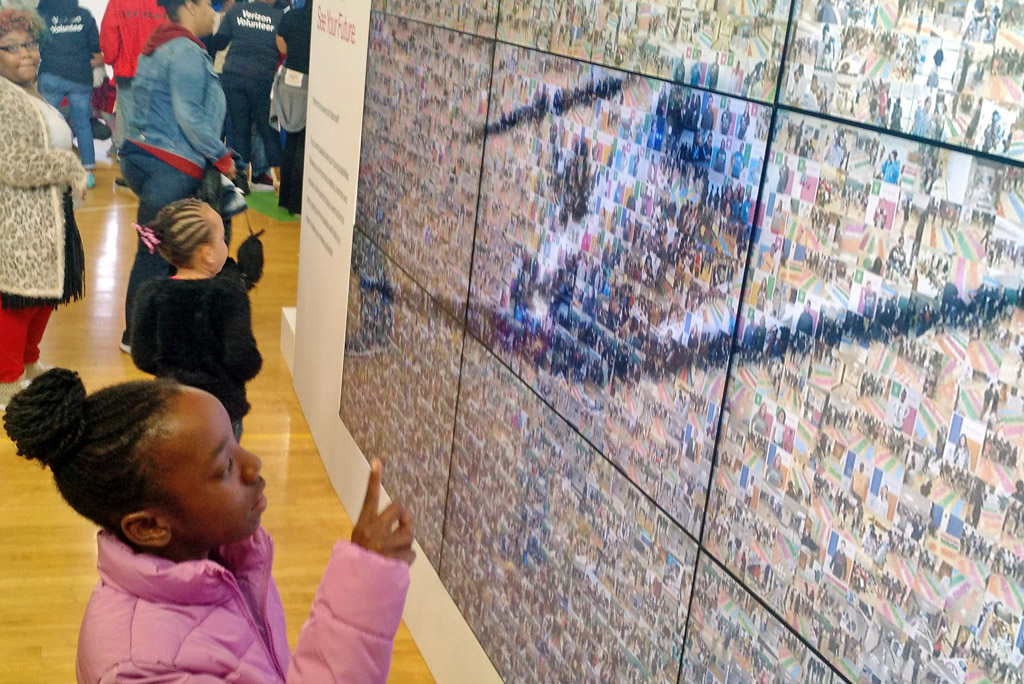 Young girl pointing at her photo in the Verizon STEM mosaic wall