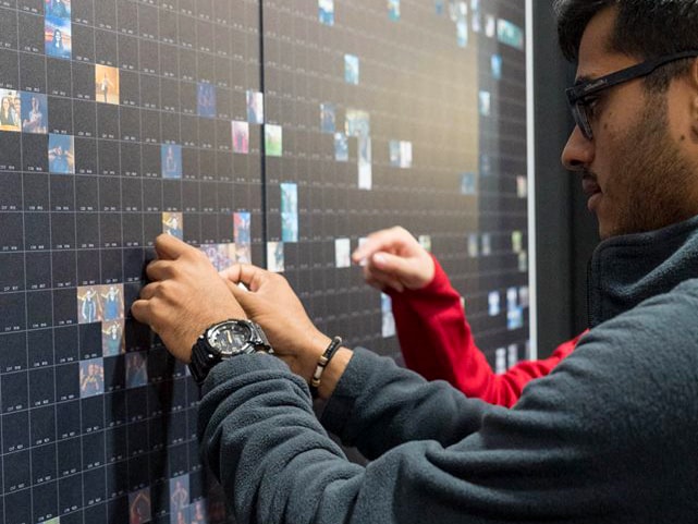 Student placing their printed photo tile onto the mosaic wall