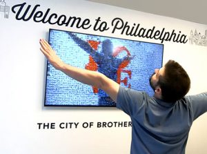 Man posing in front of a Mirror Mosaic at the Philadelphia Airport, watching as it changes as he dances