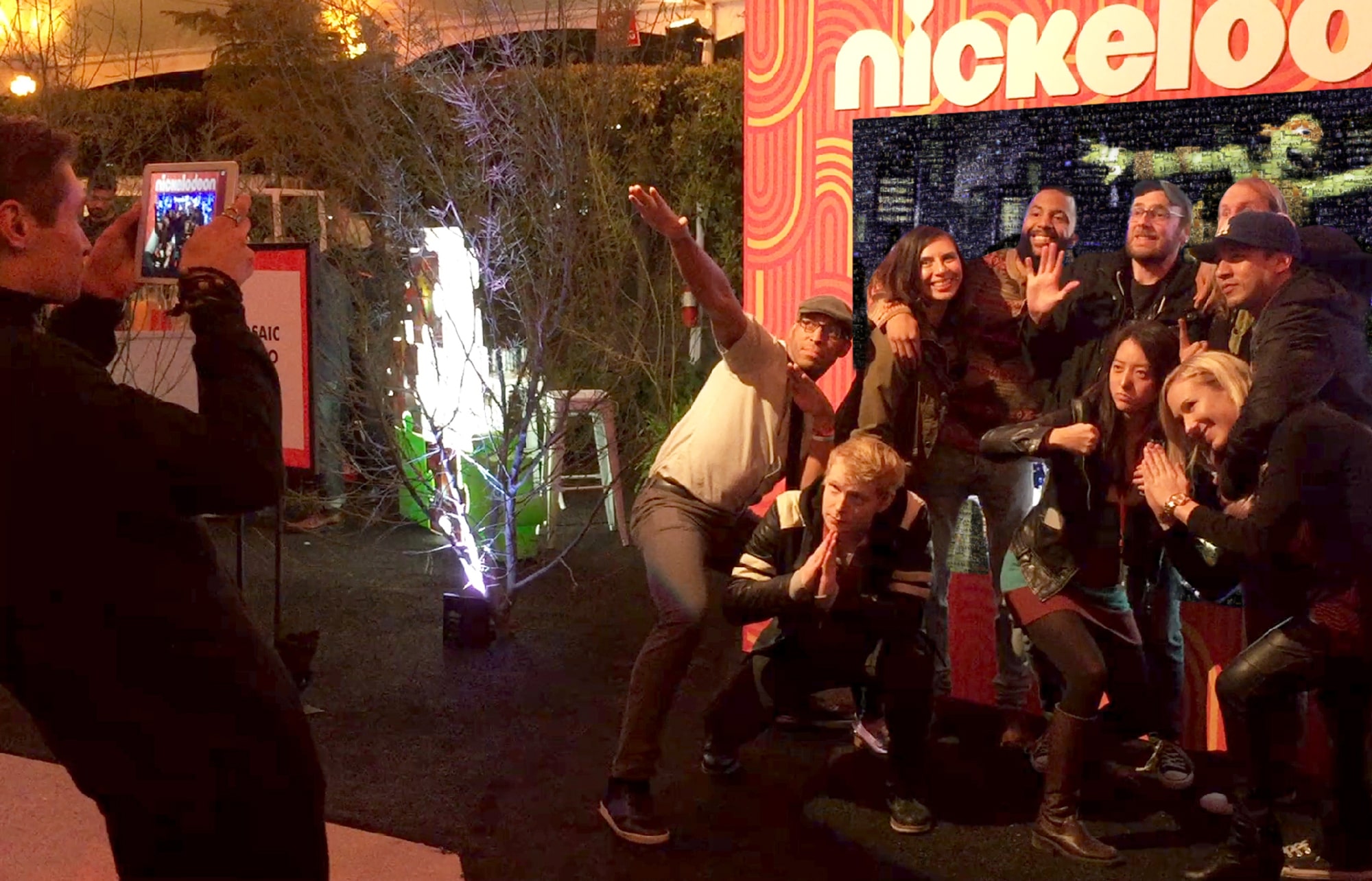 A brand ambassador takes a photo of a large group posing in front of the digital photo mosaic