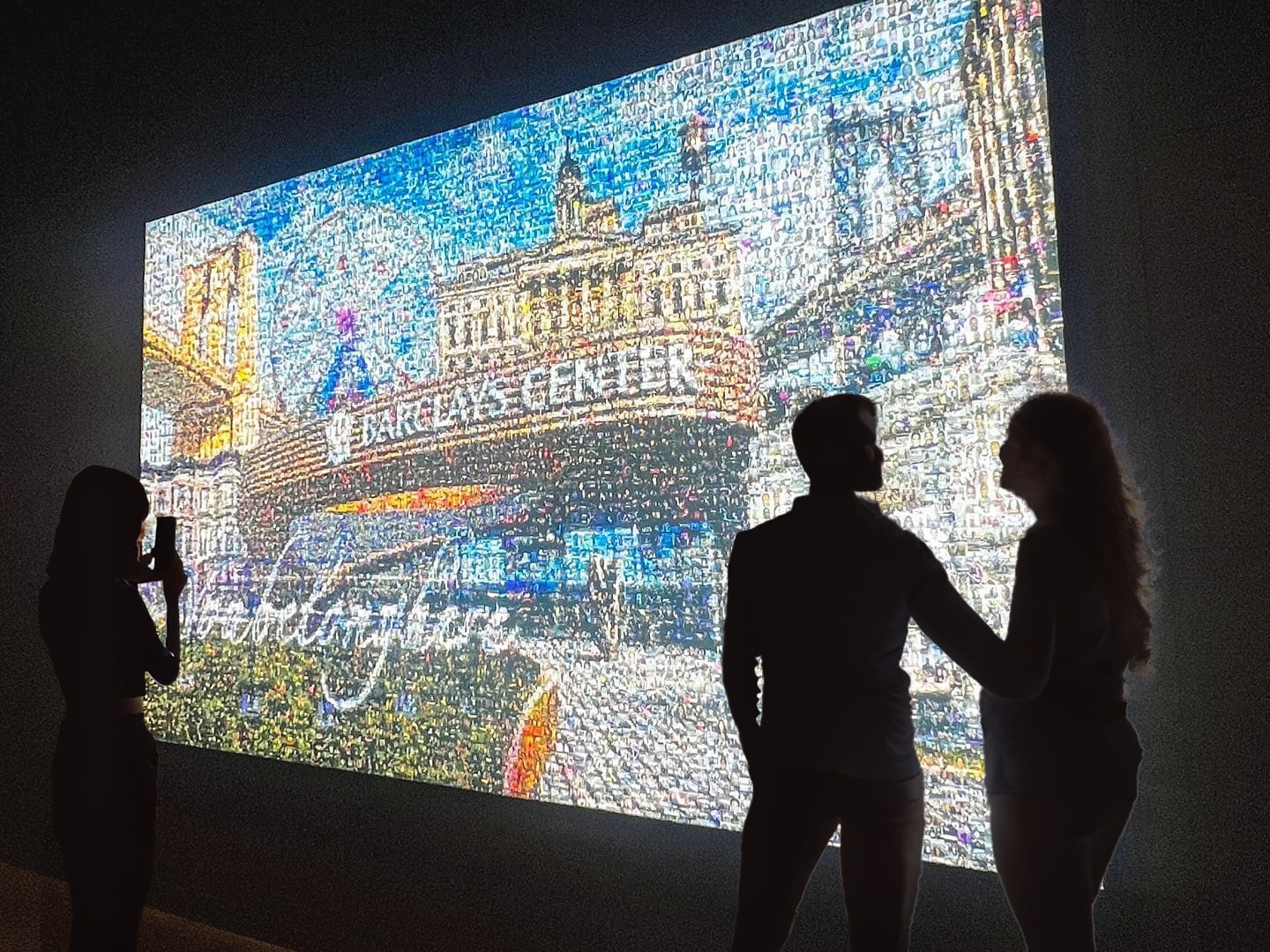 Group of guests admiring illuminated backlit photo mosaic mural at event