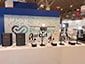 Printers, SketchBots and selfie kiosks set up on a table at an event, with a partially built SketchBot Mosaic in the background