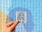 Close-up of a sketched portrait tile, held up in front of a colorful photo mosaic filled with portraits