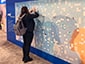Person applying an adhesive sketch onto a photo mosaic wall filled with many unique sketched portraits