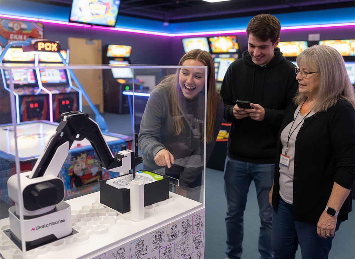 A family watching as the SketchBot creates a personalized caricature sketch
