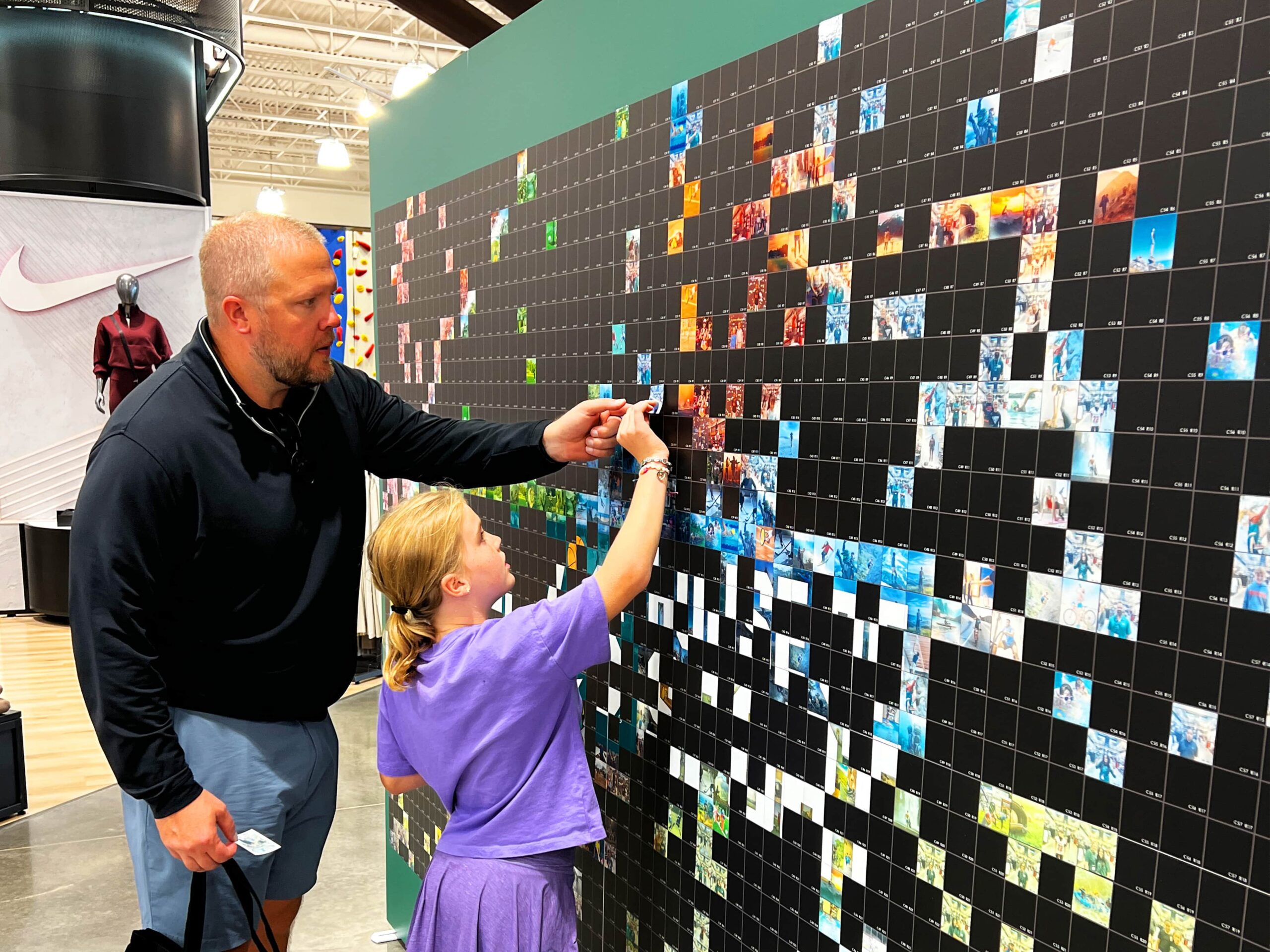 A father and daughter placing their photo tile on the mosaic wall
