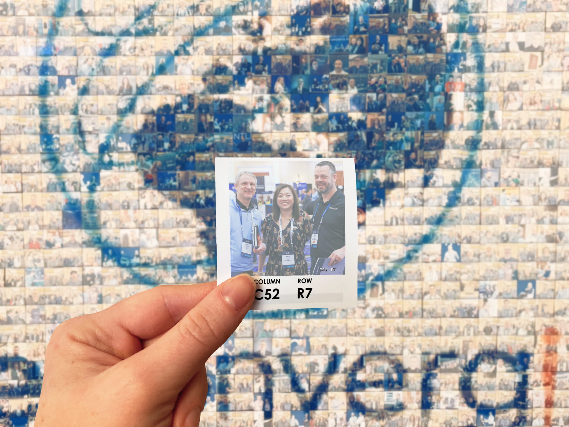 A guest holding their photo in front of the photo mosaic wall