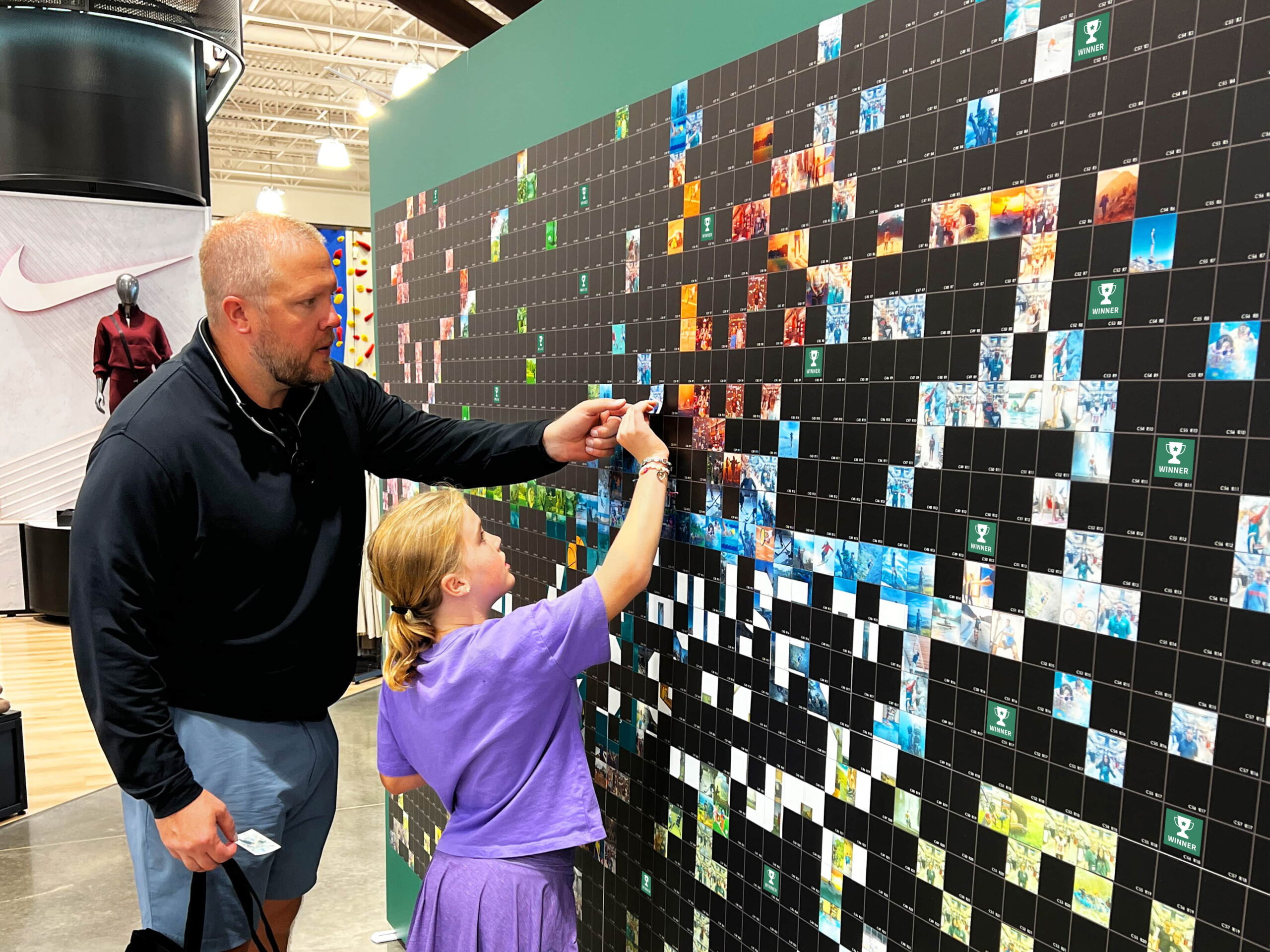 A father and daughter placing their photo tile on the mosaic wall