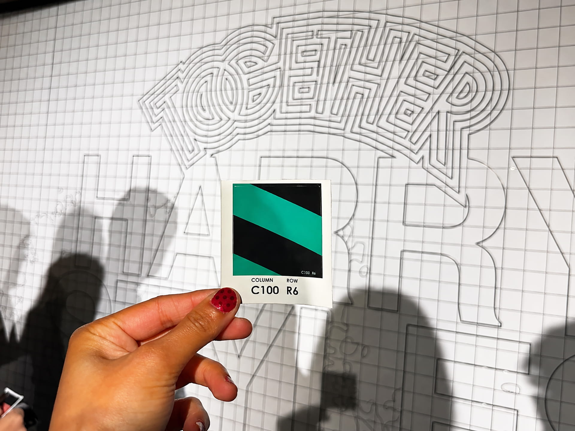 A hand holding up a sticker that will be added to the mosaic wall